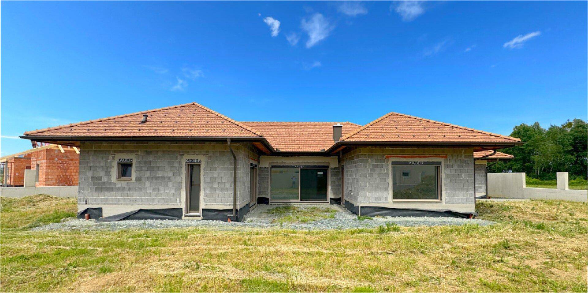 Rückansicht eines neuen Einfamilienhauses mit großen Fenstern und Ziegeldach in Bauphase.