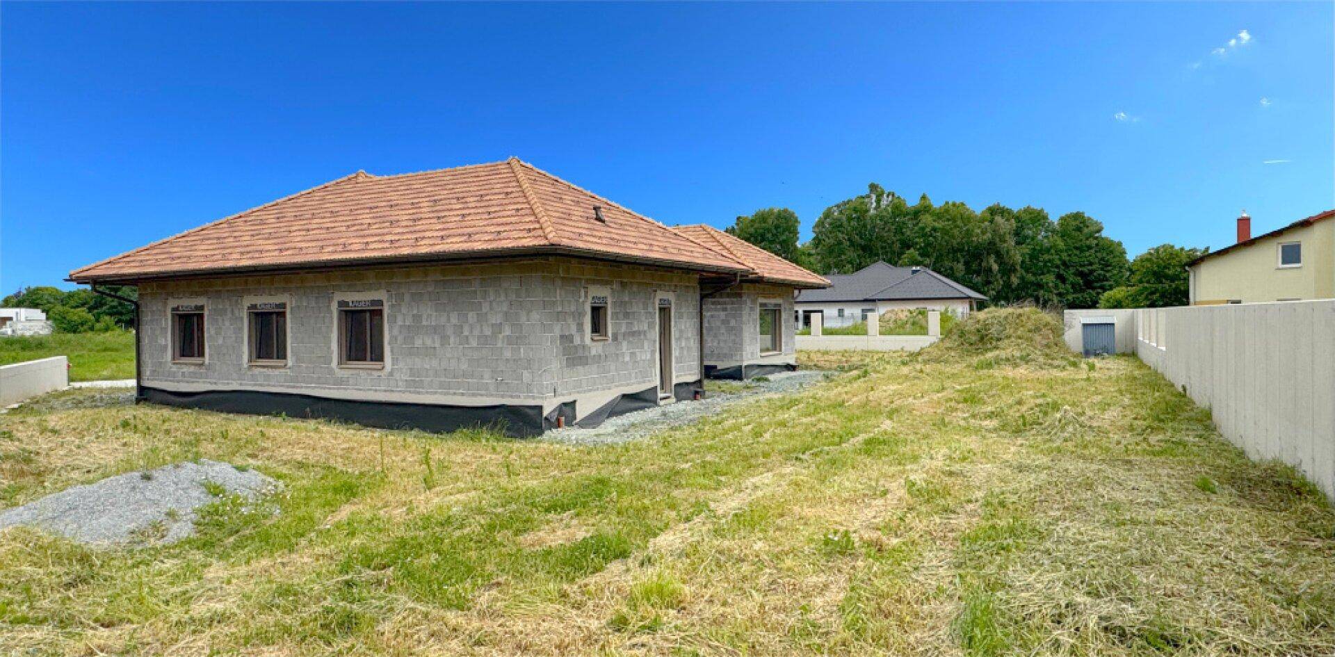 Seitenansicht eines im Bau befindlichen Einfamilienhauses mit Ziegeldach und weitem Blick.