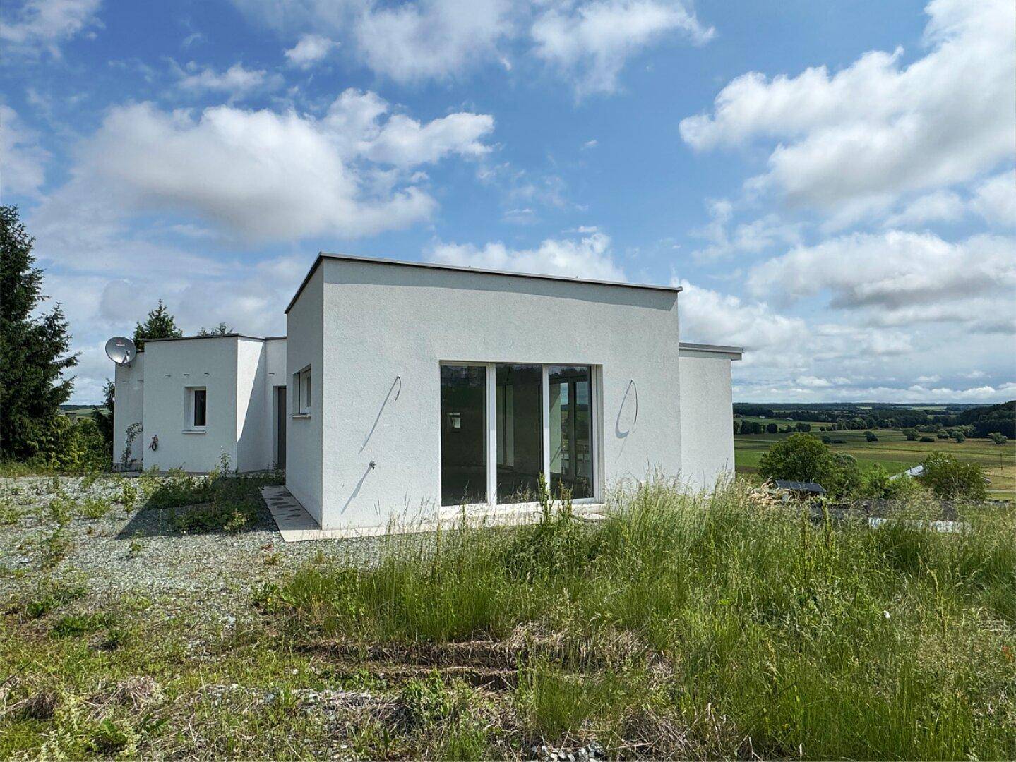 Seitenansicht des modernen Hauses mit großen Glasschiebetüren und Blick ins Grüne.