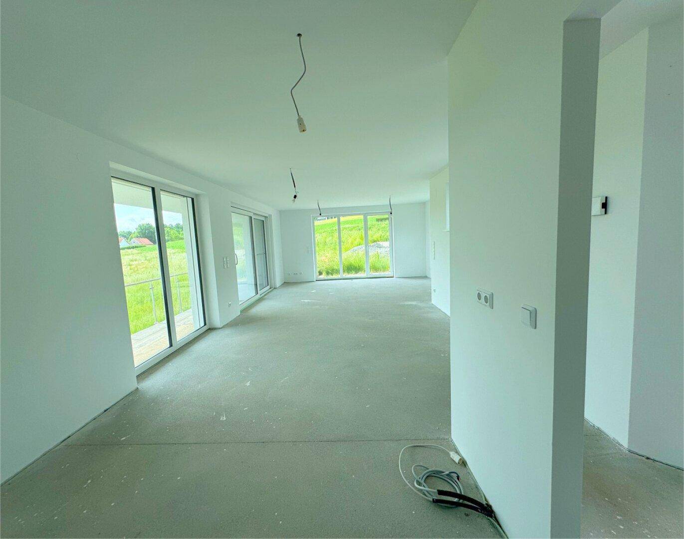 Offener Wohnbereich mit viel Tageslicht und unfertigem Boden, bereit für den Ausbau.