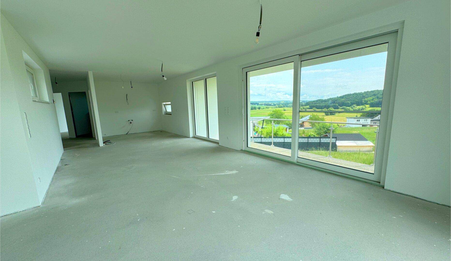Geräumiger Wohnbereich mit Schiebetüren zum Balkon und Panoramablick auf die Landschaft.