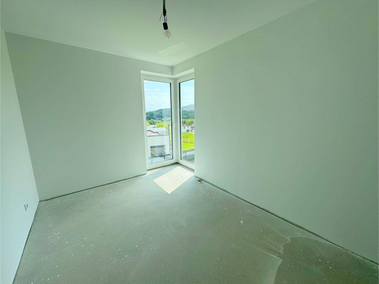 Helles Schlafzimmer mit Eckfenster und Blick auf die umliegende grüne Landschaft.