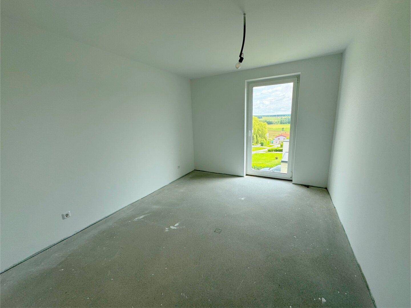 Unmöbliertes Schlafzimmer mit großem Fenster und weitem Blick ins Grüne.