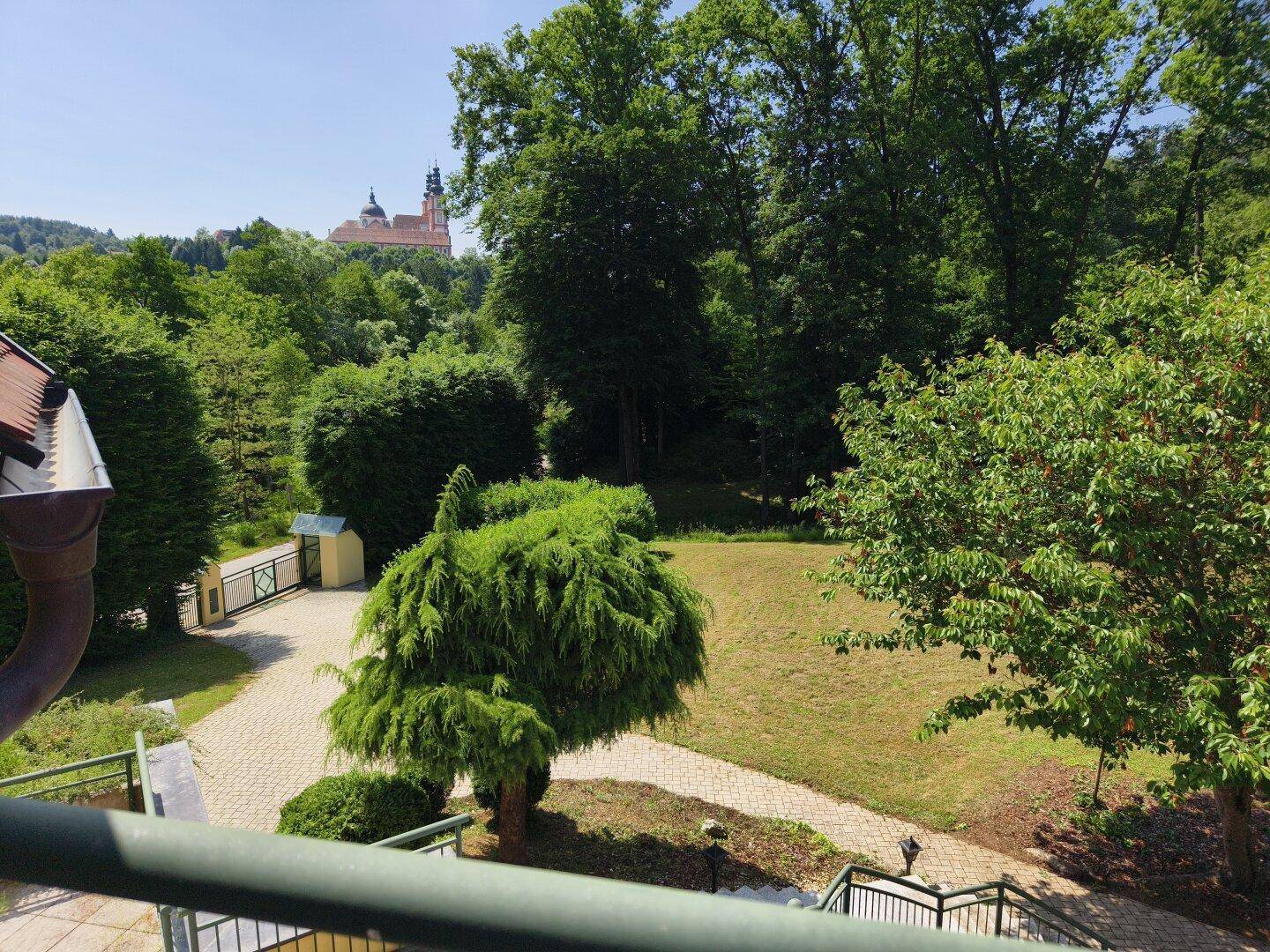 Weitläufiger Garten mit gepflasterter Auffahrt und Blick auf ein historisches Gebäude in der Ferne.