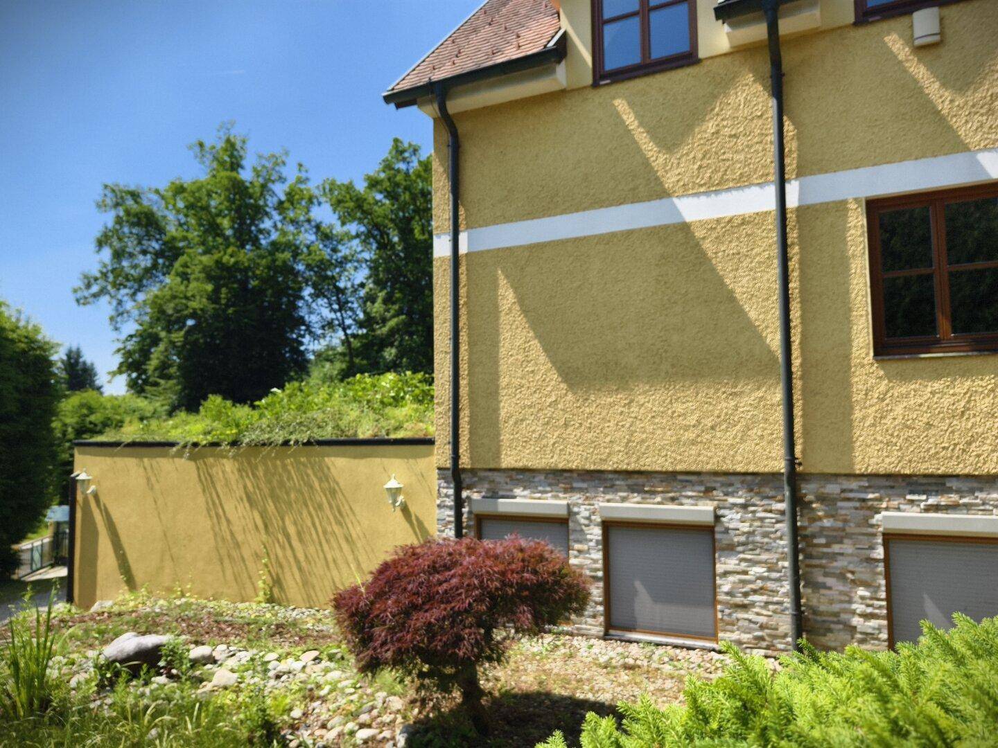 Seitenansicht des Hauses mit Steinfassade im unteren Bereich und einem begrünten Dach.