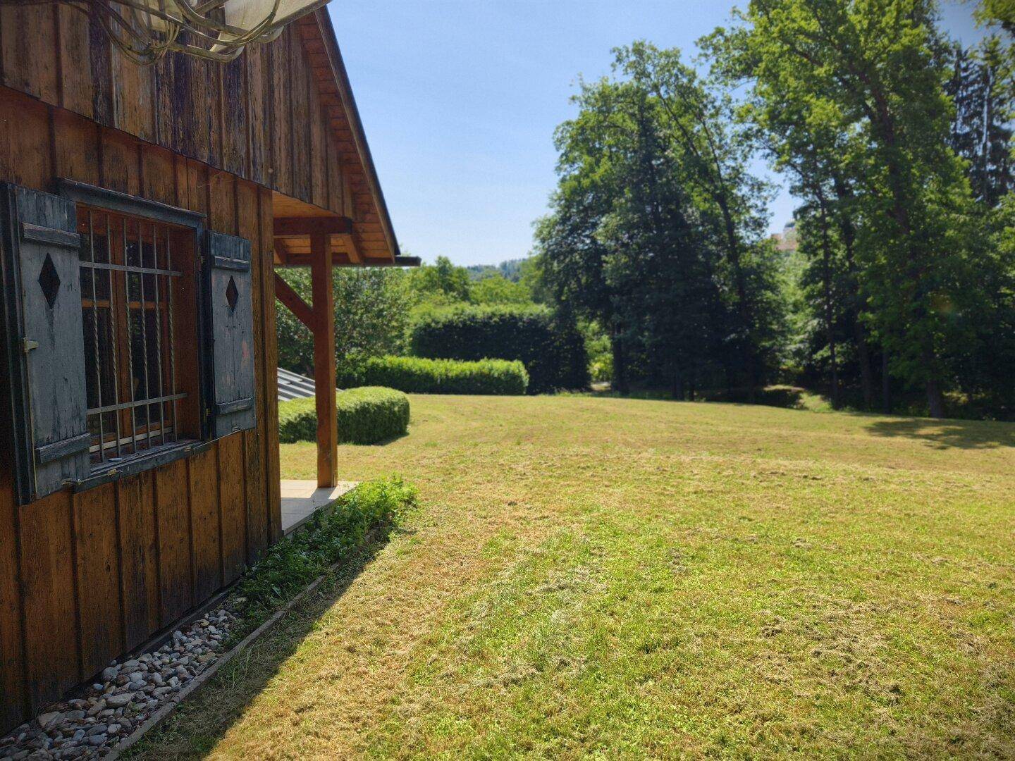 Rustikales Holzhaus mit großer Rasenfläche und Blick auf die grüne Landschaft.