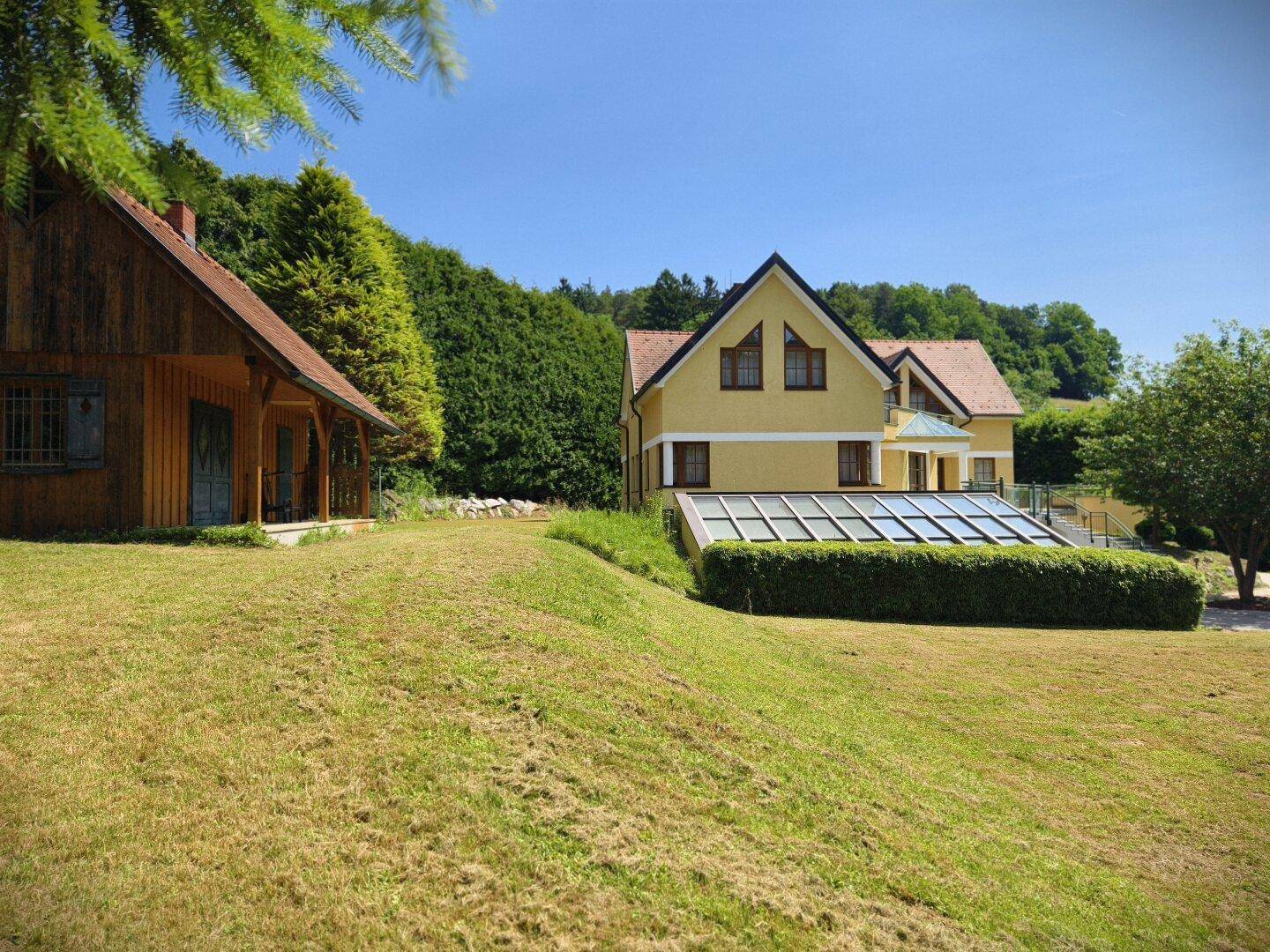 Weitläufiger Gartenbereich mit Haupthaus und Holzchalet, umgeben von grüner Natur.