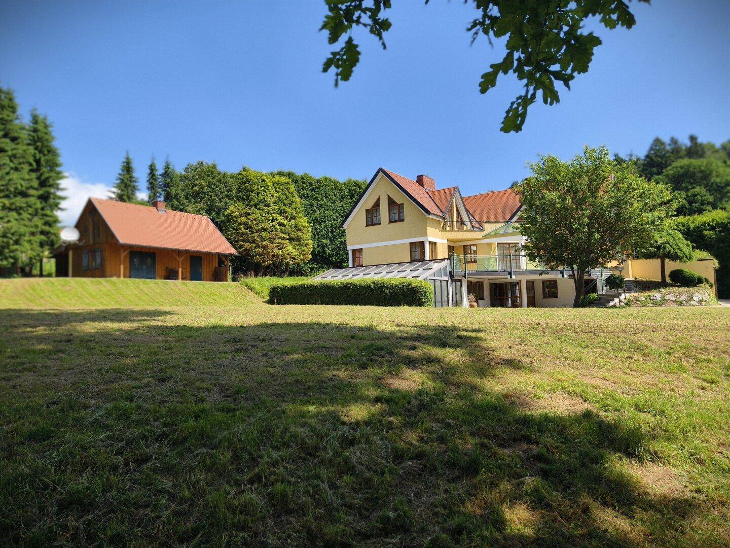 Großzügige Grünfläche mit Haupthaus und Holzchalet unter strahlend blauem Himmel.