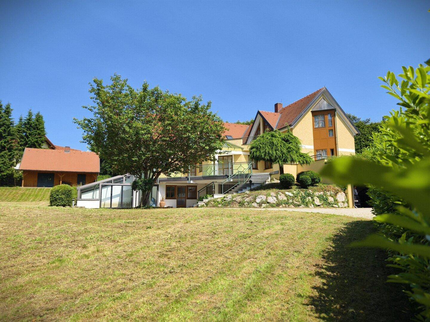 Haupthaus und Holzchalet in einer weitläufigen Gartenlandschaft mit gepflegtem Rasen.