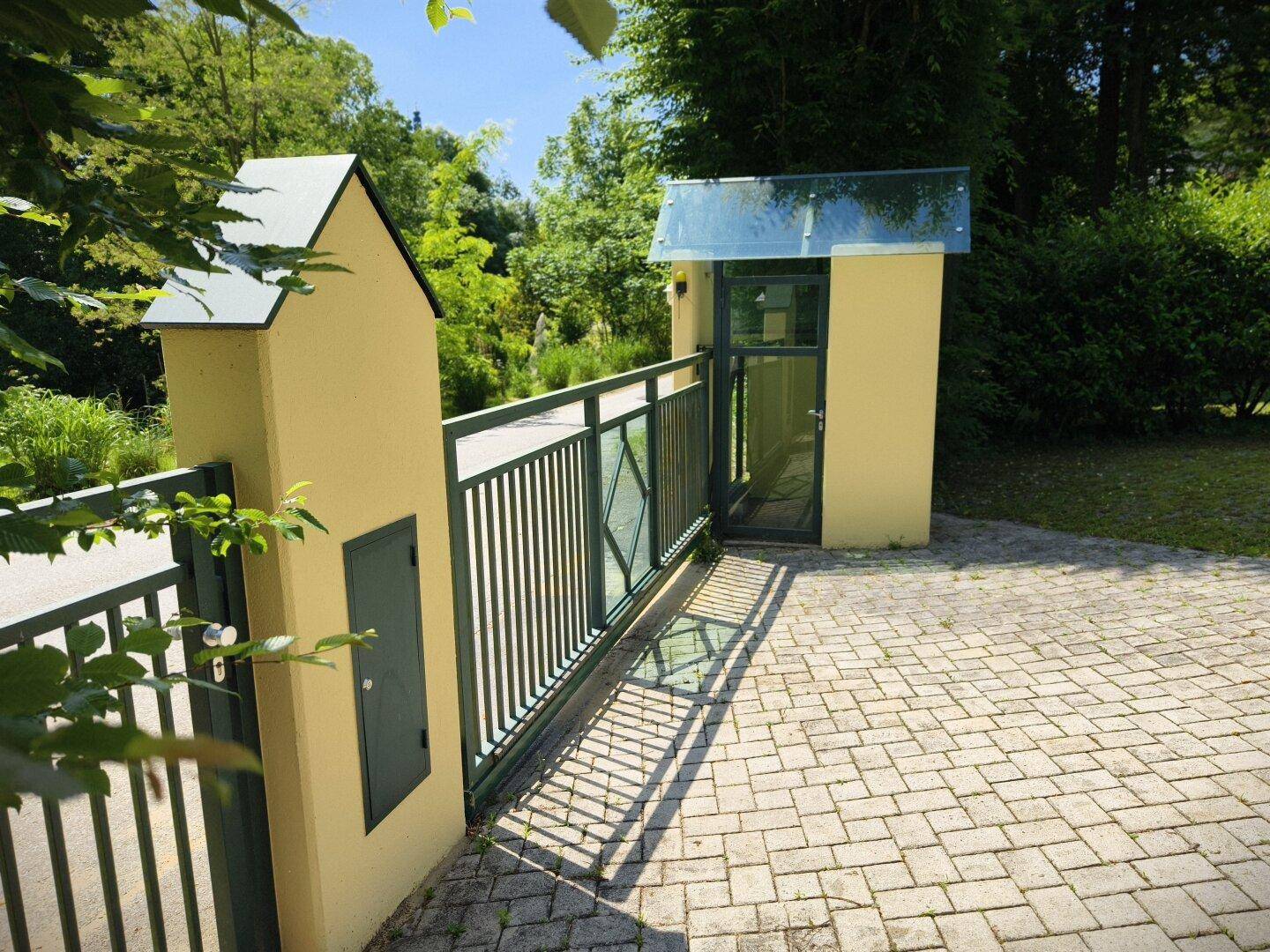 Modernes Eingangstor mit Glasdetails und gepflastertem Zugangsbereich.