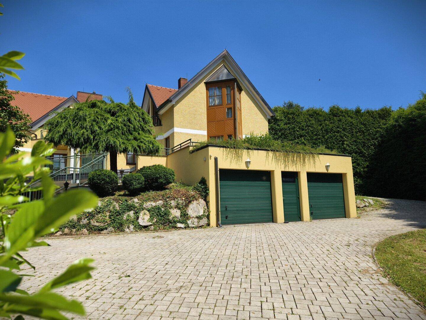 Haupthaus mit dreifacher Garage und gepflasterter Auffahrt, umgeben von Grün.