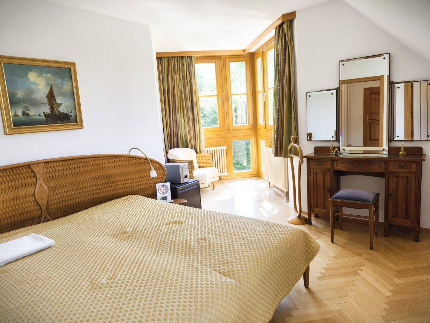 Gemütliches Schlafzimmer mit Holzparkett, großen Fenstern und einem antiken Schminktisch.