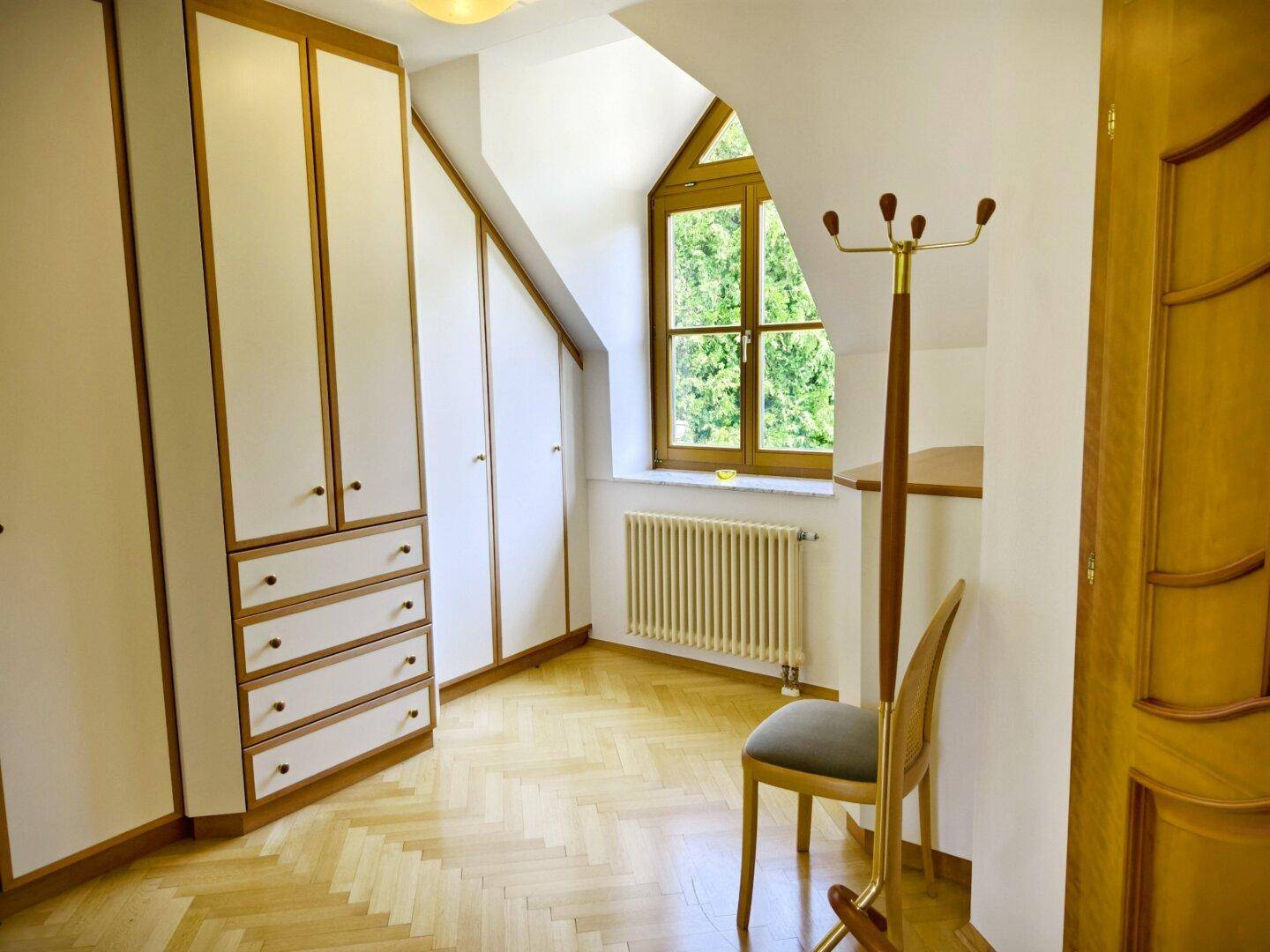 Kleines Zimmer mit Einbauschränken, Holzparkett und Fenster mit Blick ins Grüne.