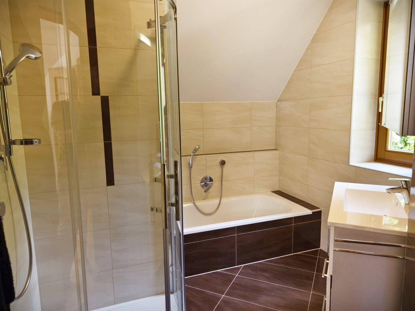 Modernes Badezimmer mit Duschkabine, Badewanne und Fenster unter der Dachschräge.
