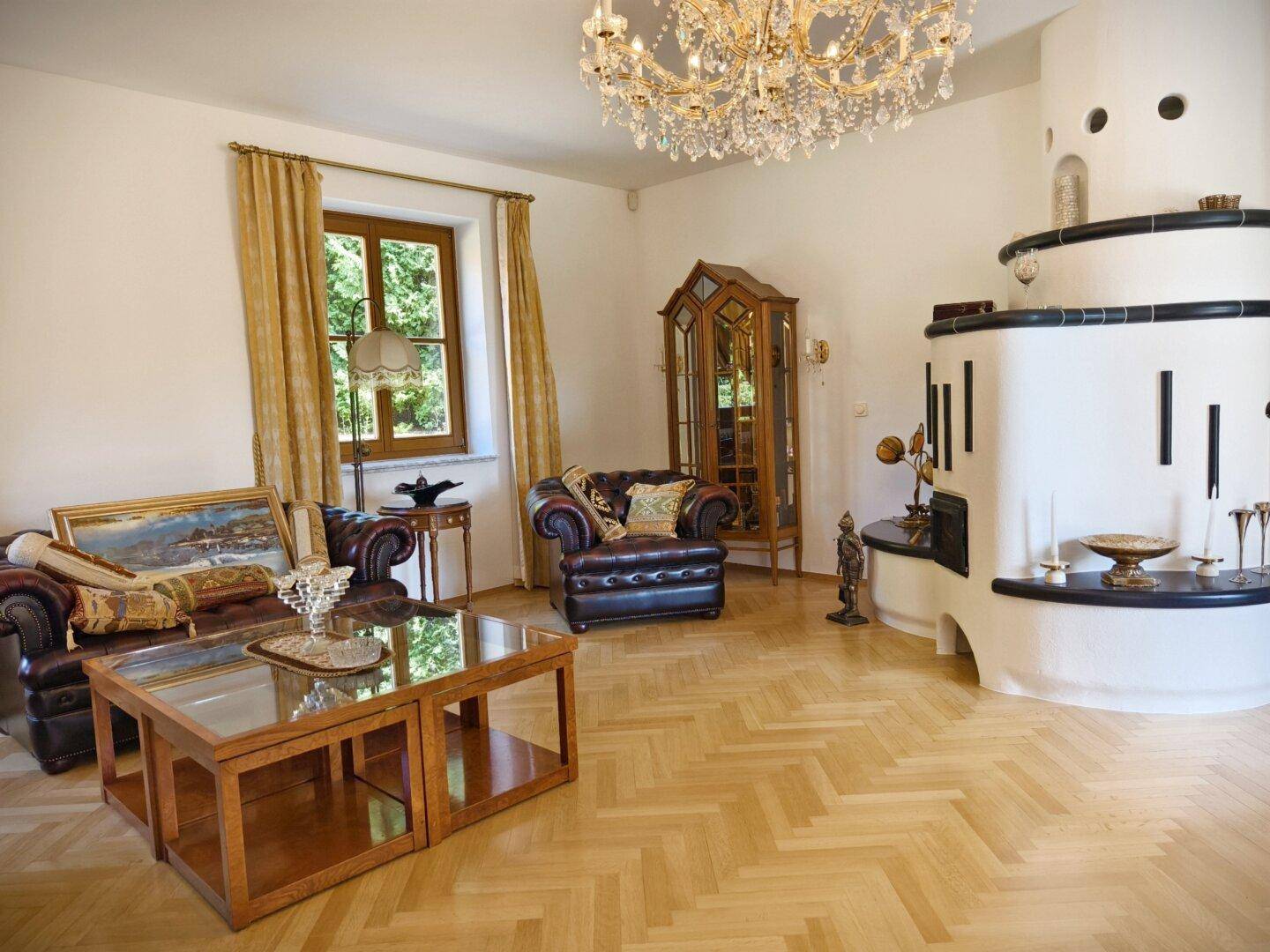 Elegantes Wohnzimmer mit Kachelofen, Ledersesseln, Kronleuchter und Parkettboden.