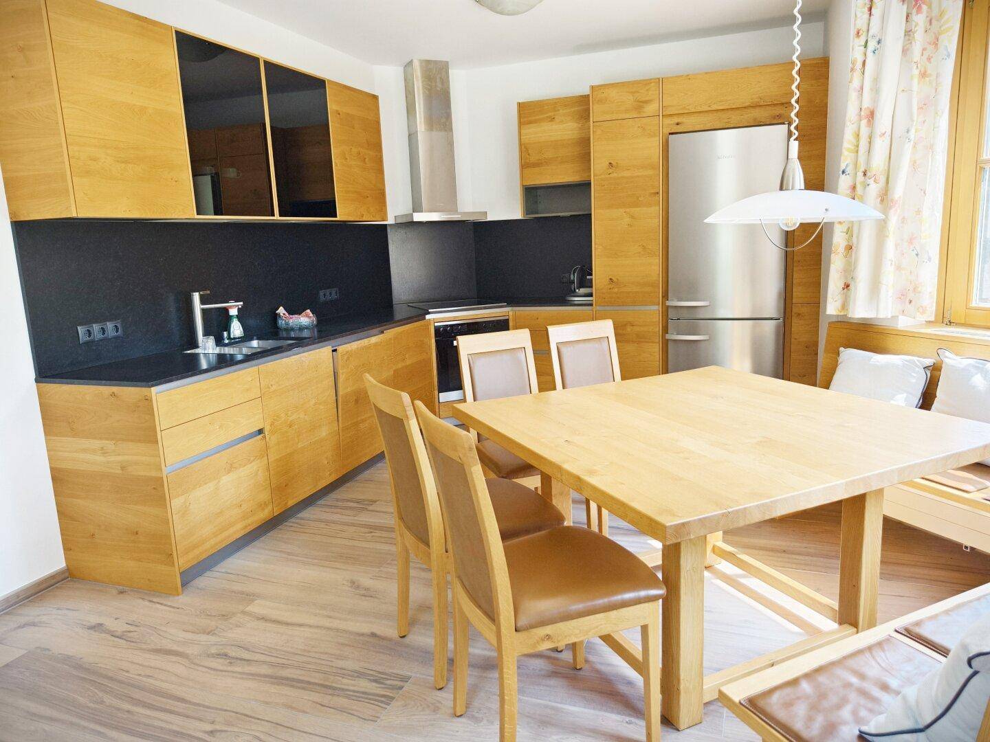 Moderne Holzküche mit Essbereich, schwarzen Arbeitsplatten und integrierten Geräten.