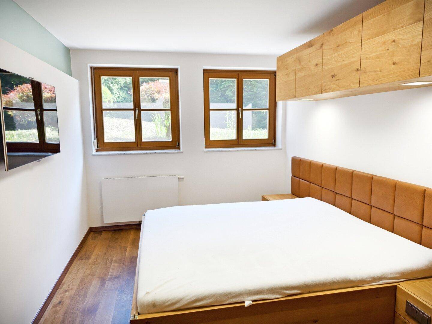 Modernes Schlafzimmer mit Holzbett, Parkettboden und Fenstern mit Blick ins Grüne.