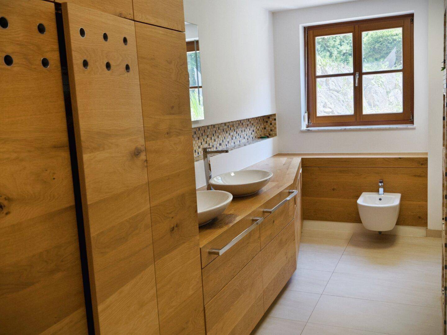 Helles Badezimmer mit Holzwaschtisch, zwei Aufsatzwaschbecken und Bidet.