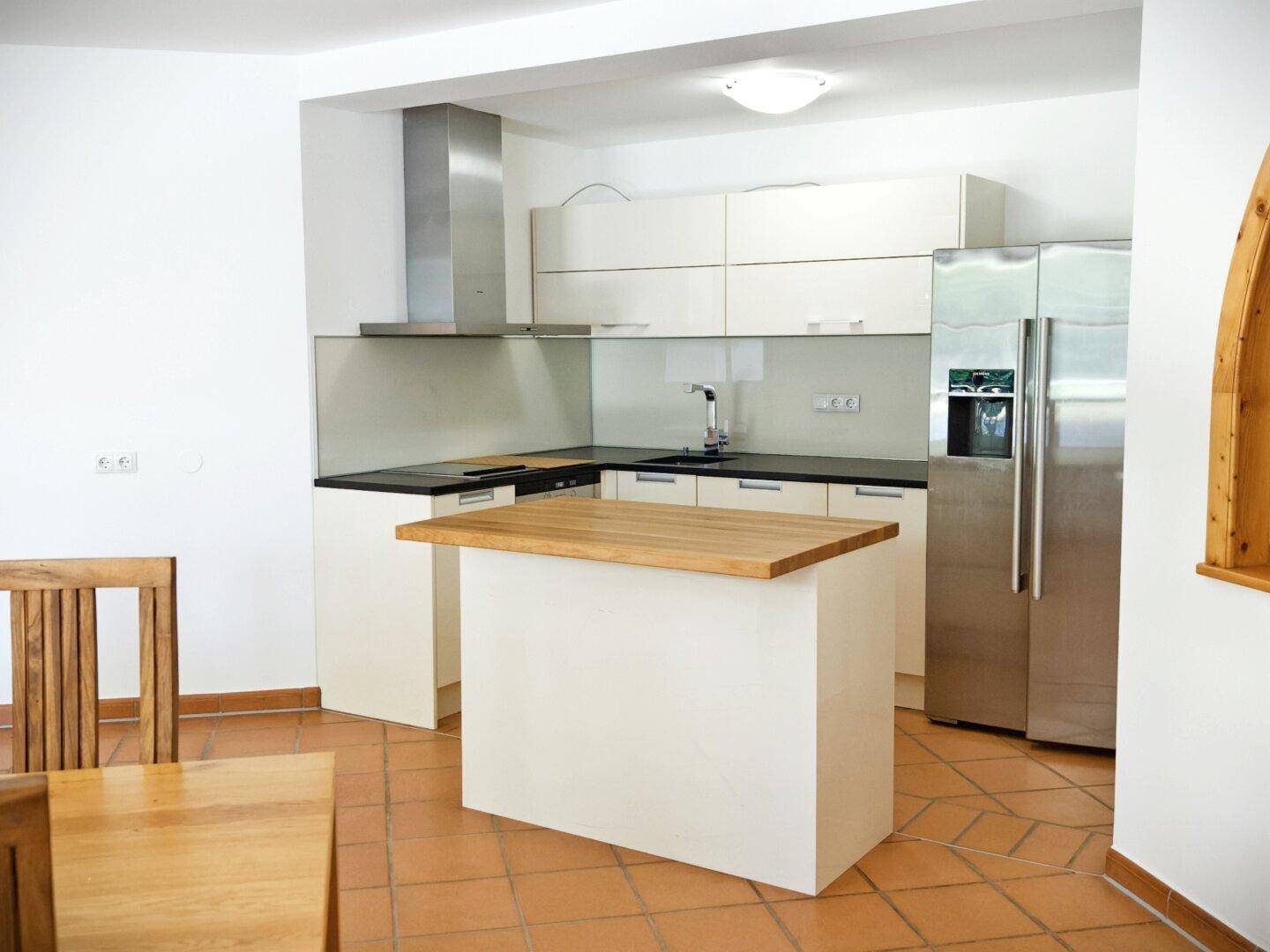Helle Küche mit Terrakottafliesen, einer Kücheninsel aus Holz und modernen Geräten.