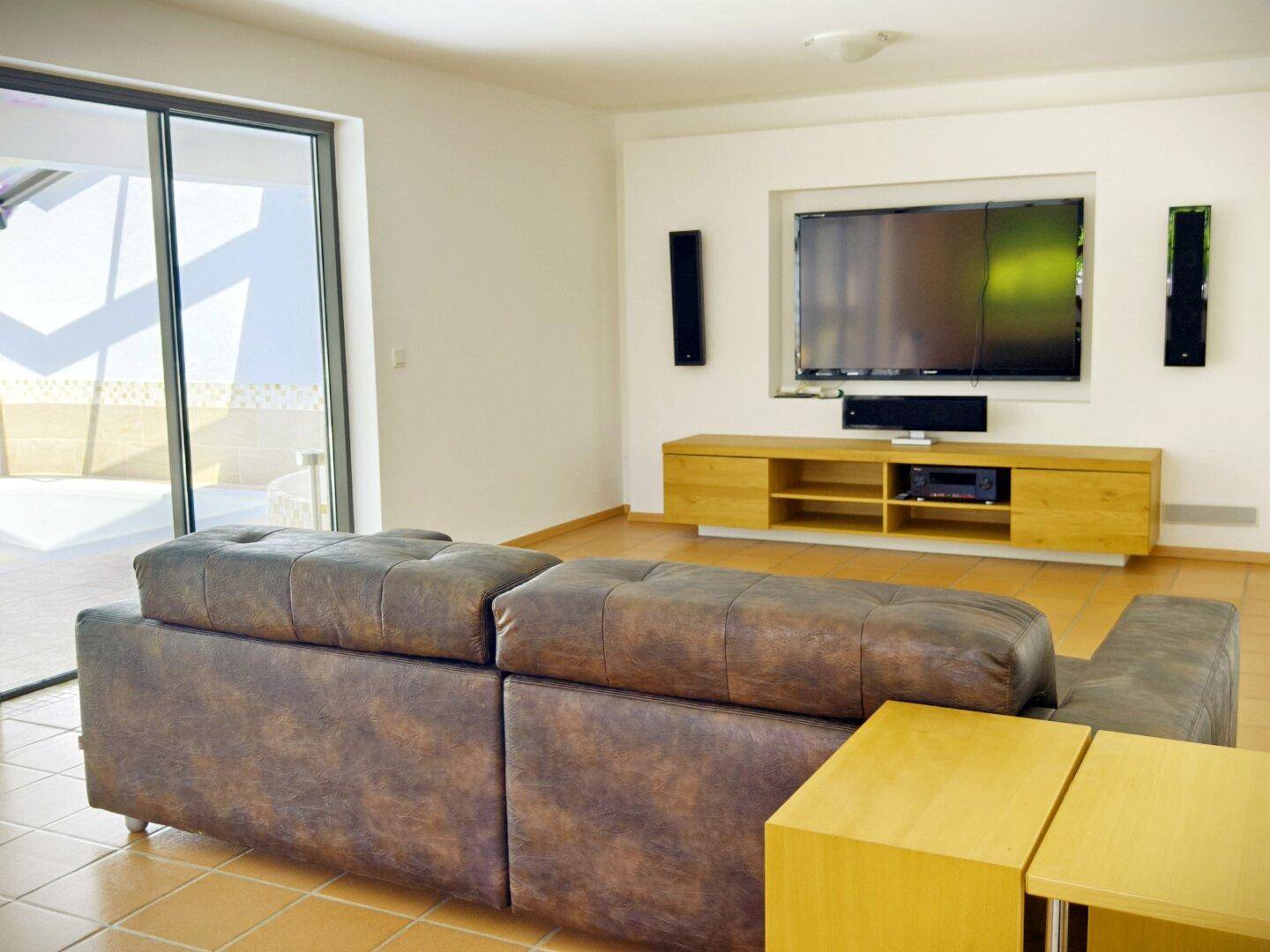 Gemütliches Wohnzimmer mit großem Sofa, Fliesenboden und Zugang zu einer Terrasse.