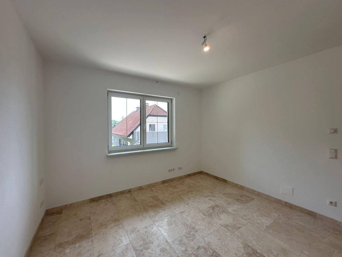 Geräumiges Schlafzimmer mit Fliesenboden und Fenster, das einen Blick auf ein Nachbarhaus ermöglicht.