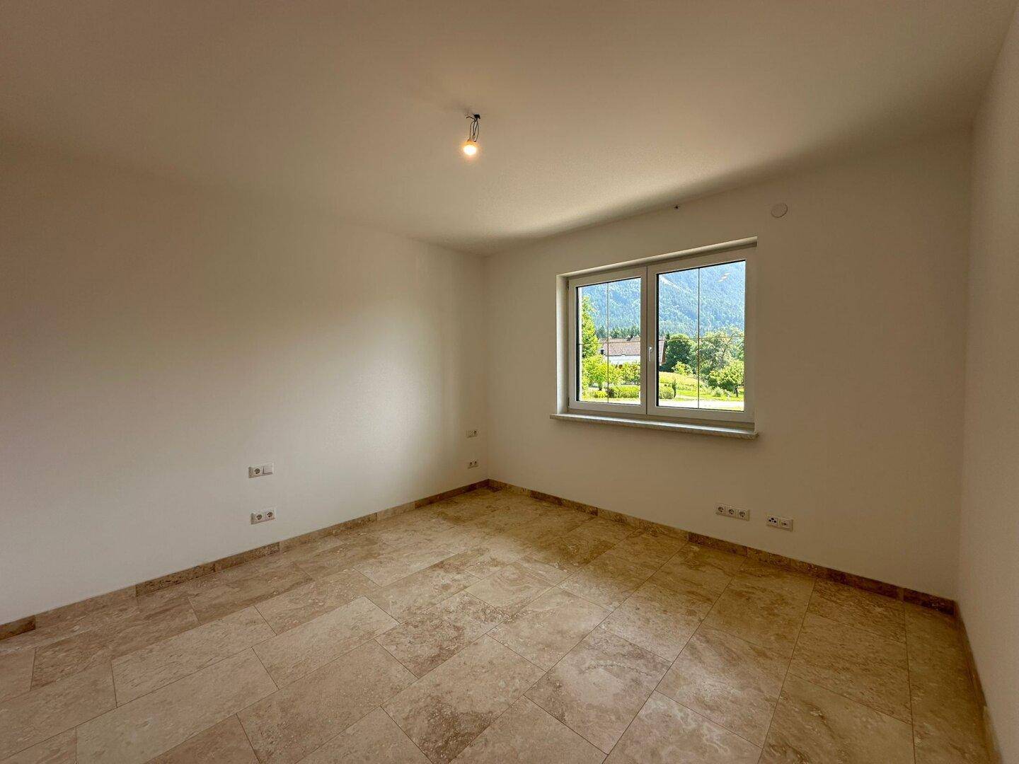 Helles Schlafzimmer mit Fliesenboden und Fenster, das einen Blick auf die grüne Umgebung bietet.