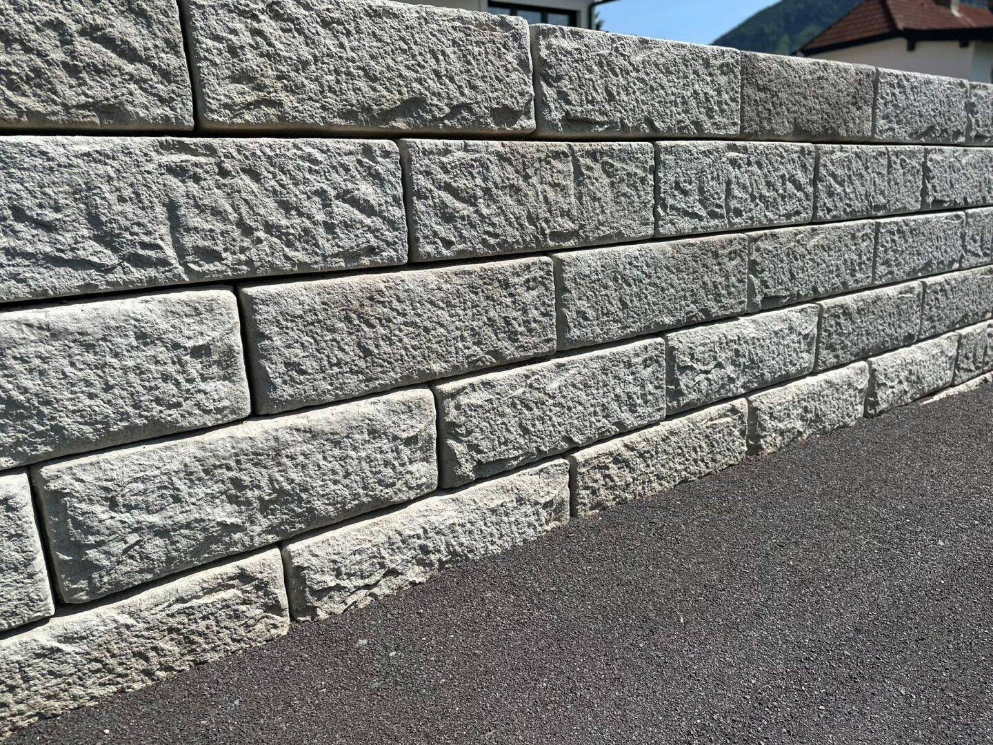 Eine robuste Stützmauer aus groben Steinblöcken, die das Gelände sichert und gut gepflegt ist.