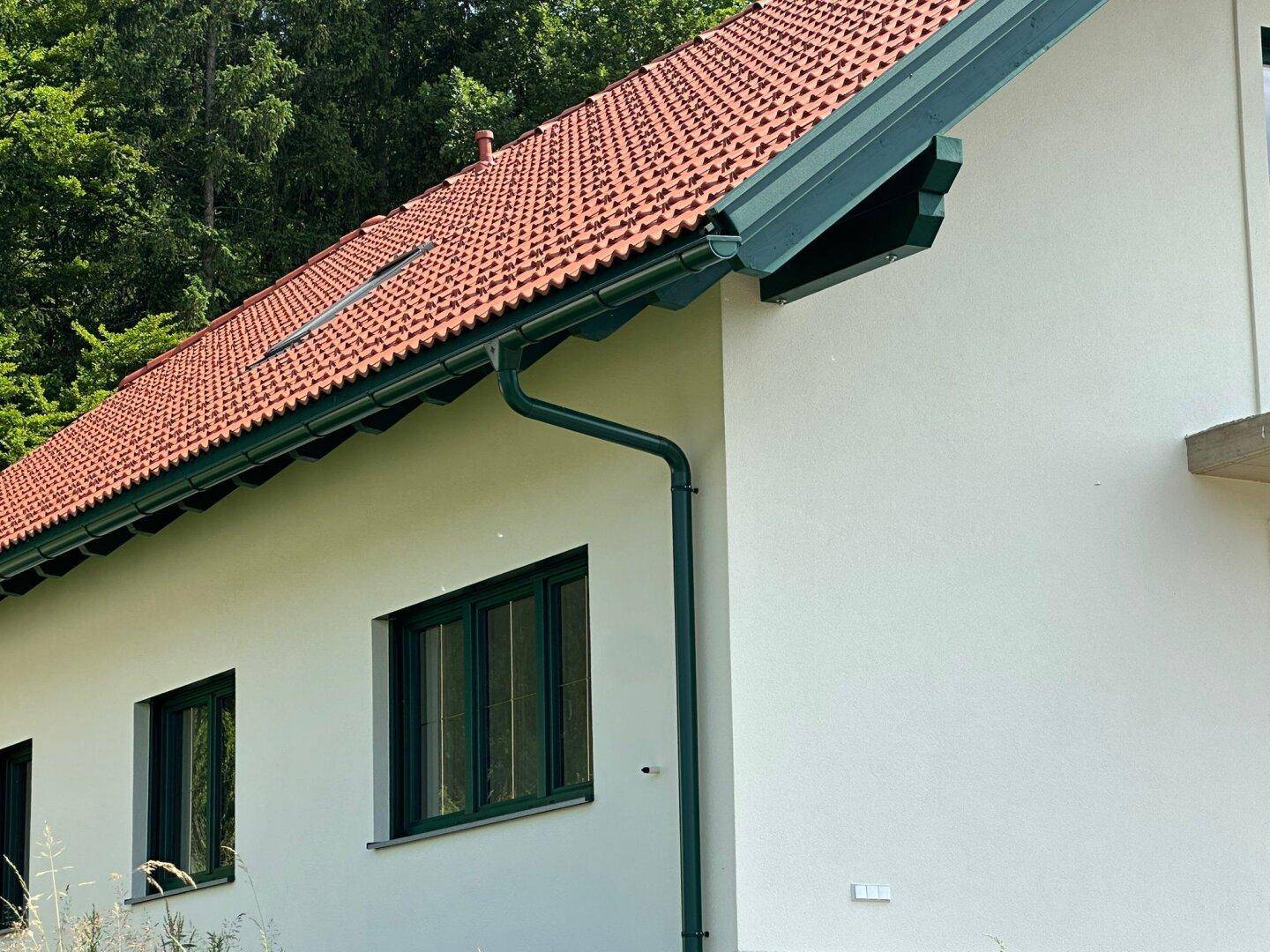 Detailansicht des roten Ziegeldachs und der grünen Regenrinne eines modernen Einfamilienhauses.