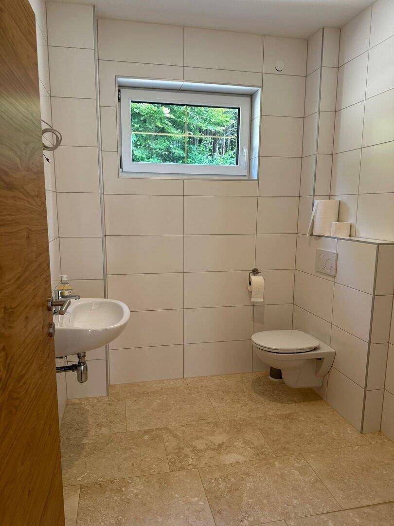 Helles Gäste-WC mit weißen Fliesen, wandmontierter Toilette und kleinem Waschbecken.