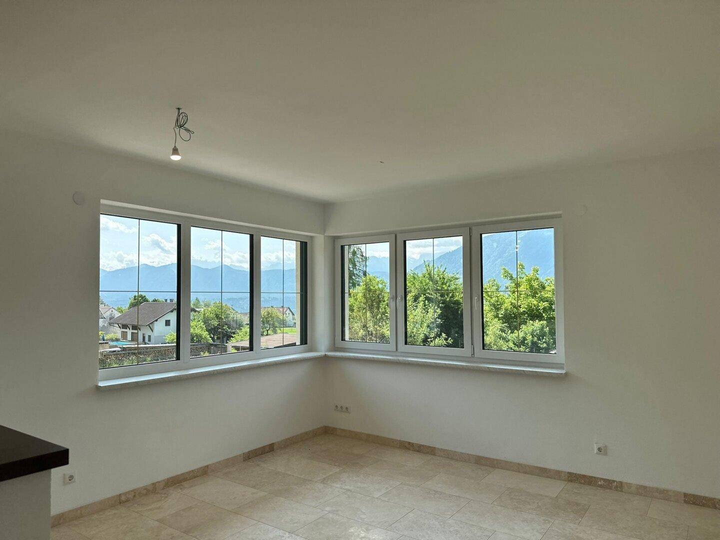 Heller Wohnbereich mit großen Fenstern, Fliesenboden und weitem Blick auf die Berge und Landschaft.