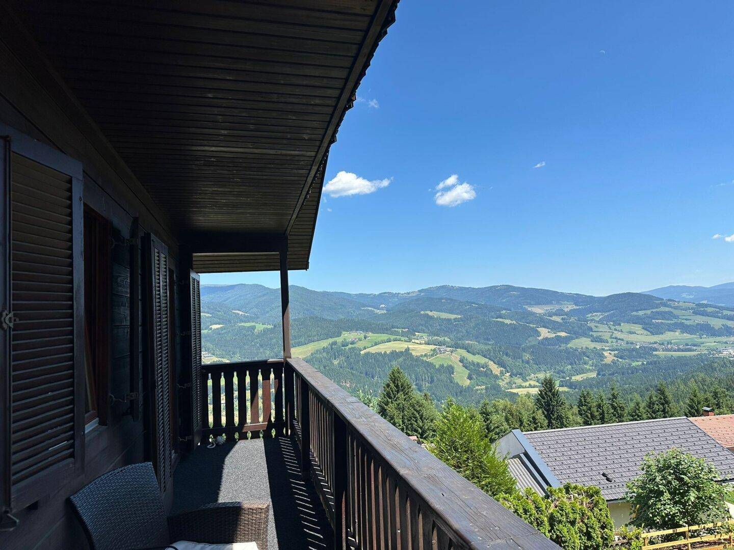 Panoramablick vom Balkon über die weite, grüne Hügellandschaft und die majestätischen Berge.