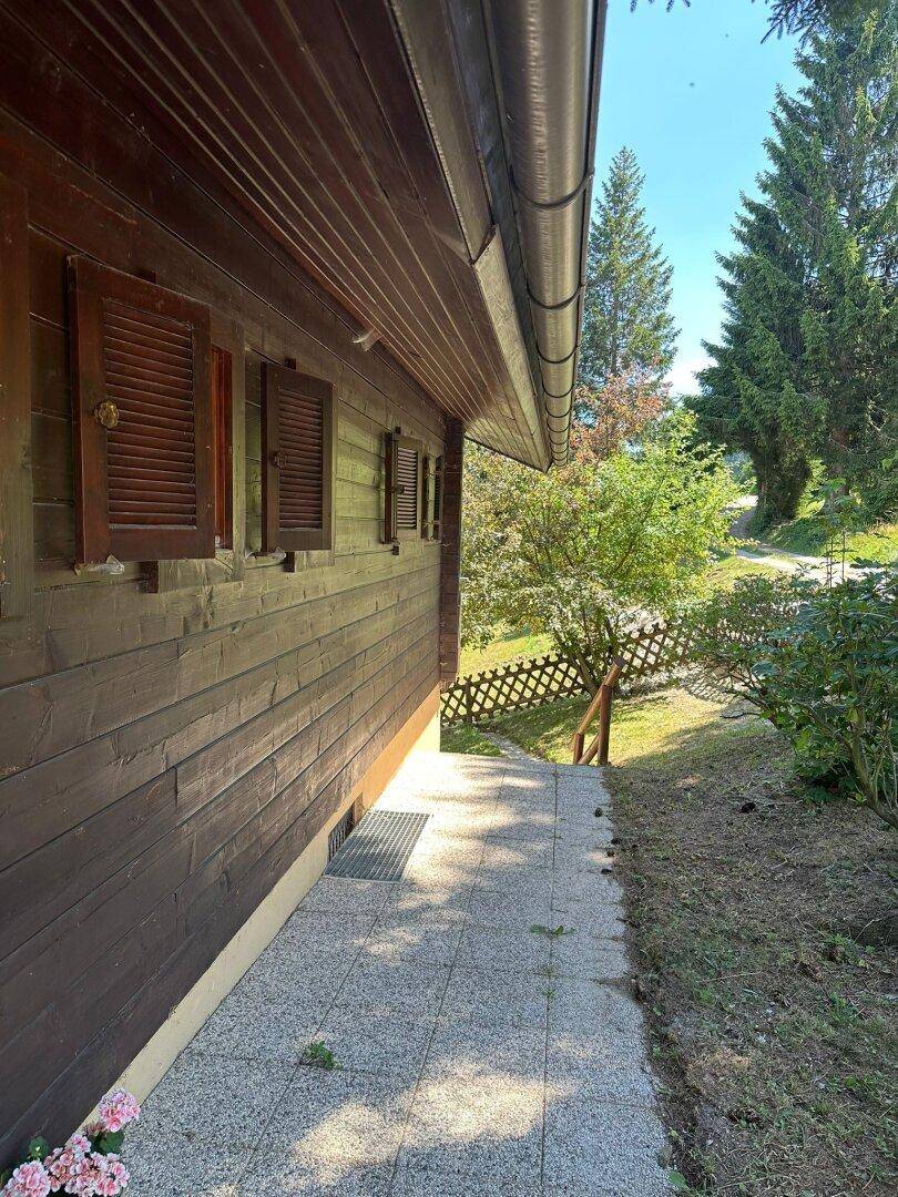 Detailansicht der dunklen Holzfassade mit traditionellen Fensterläden und einem gepflasterten Zugangsbereich.