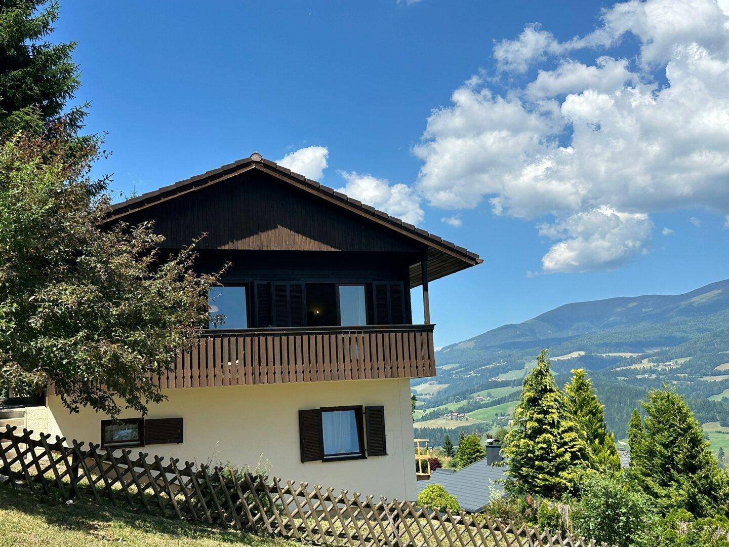 Charmantes Haus mit traditioneller Holzfassade und einem Balkon, der einen weiten Blick auf die grüne Berglandschaft bietet.