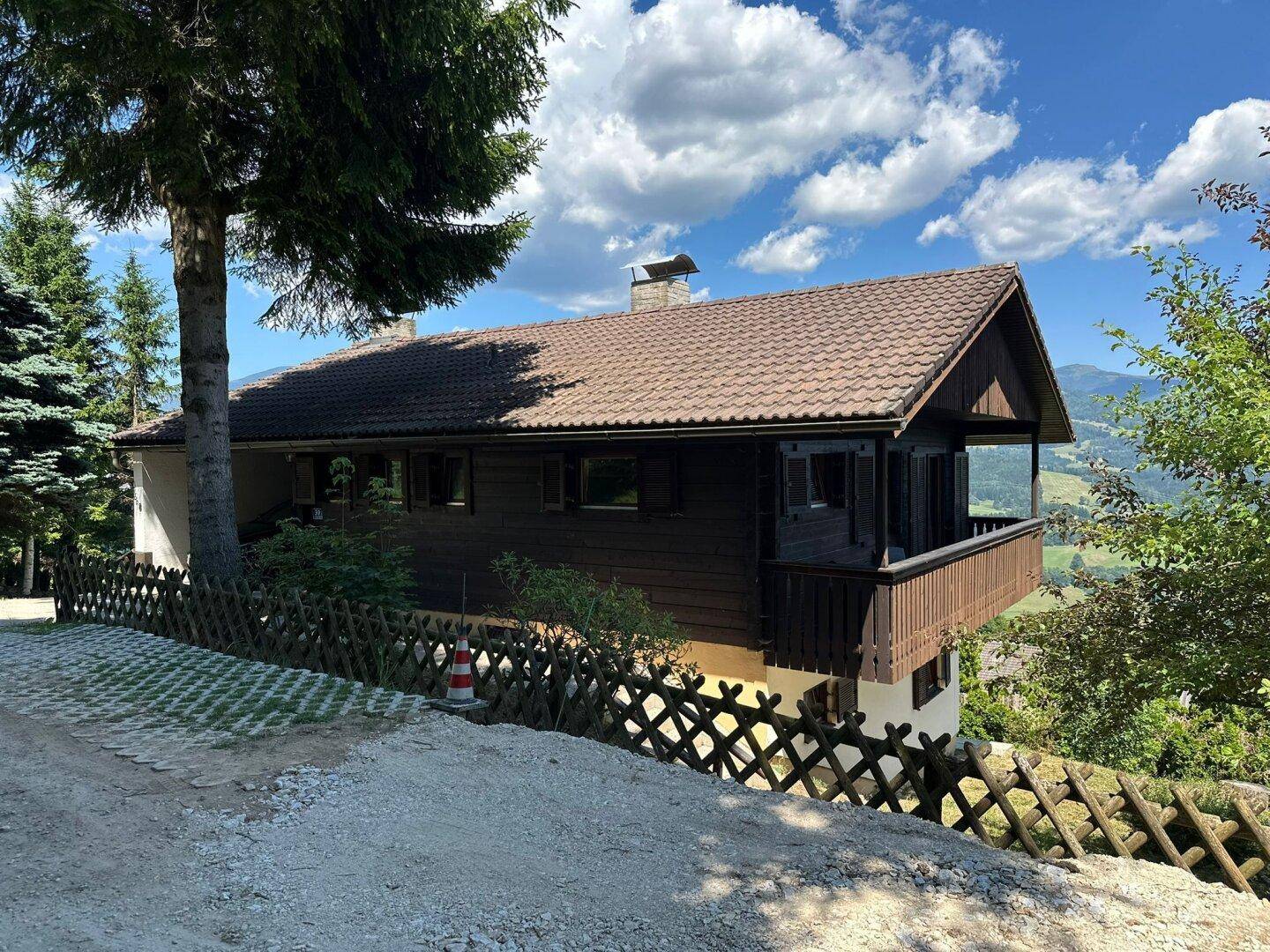 Traditionelles Haus mit Holzelementen und einem kleinen Balkon, eingebettet in eine malerische Berglandschaft.