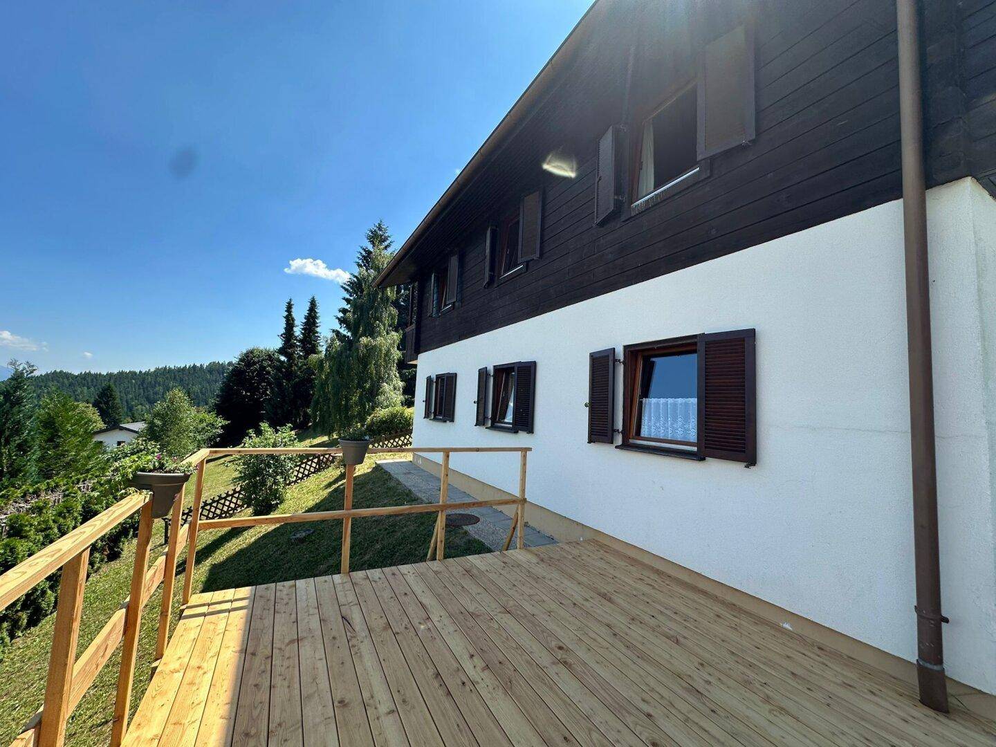 Neu errichtete Holzterrasse entlang der Hausfassade mit Blick auf die umliegende Natur und die Berge.