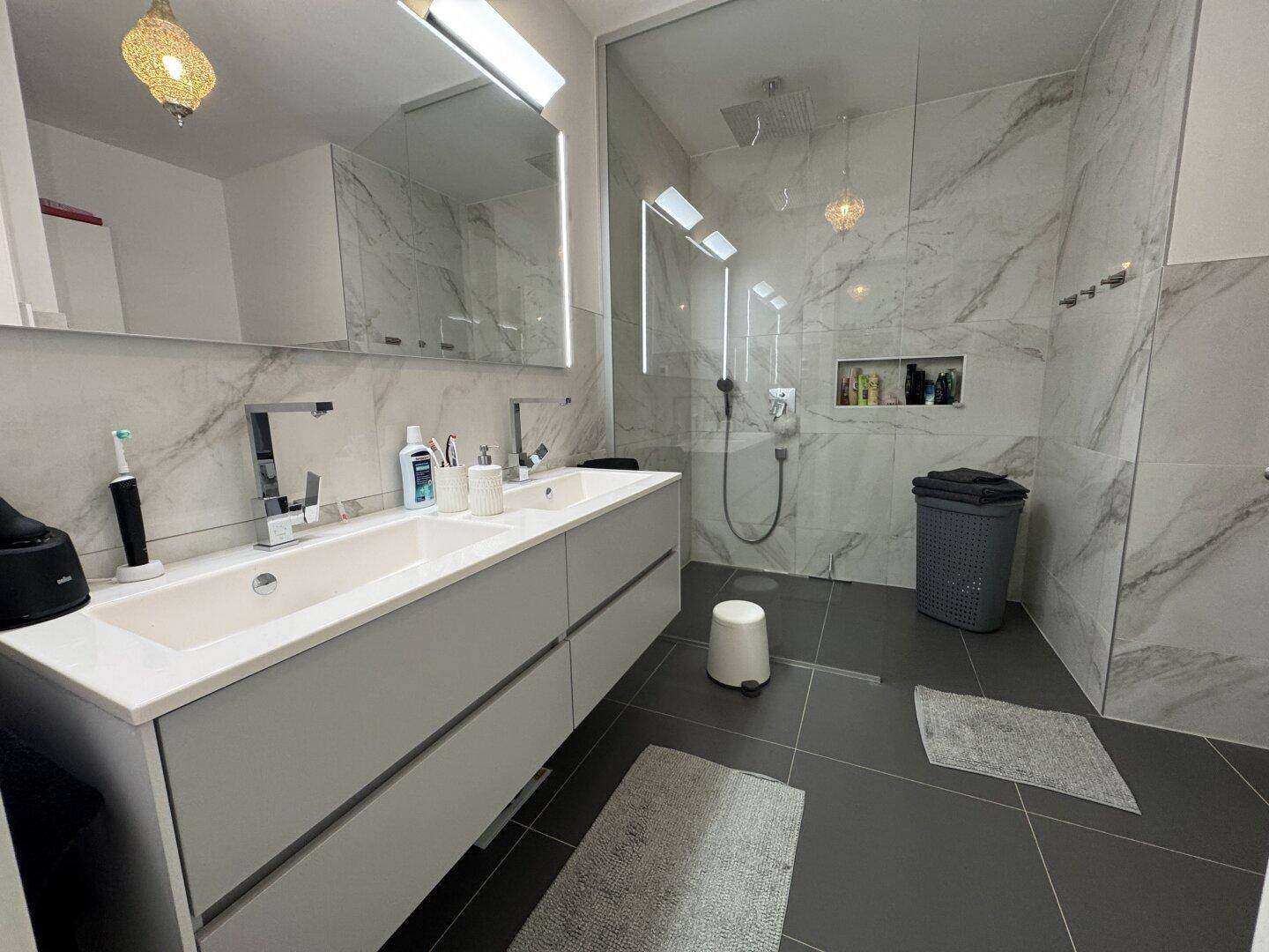 Modernes Badezimmer mit Doppelwaschbecken, großer begehbarer Dusche und eleganten Marmorfliesen.
