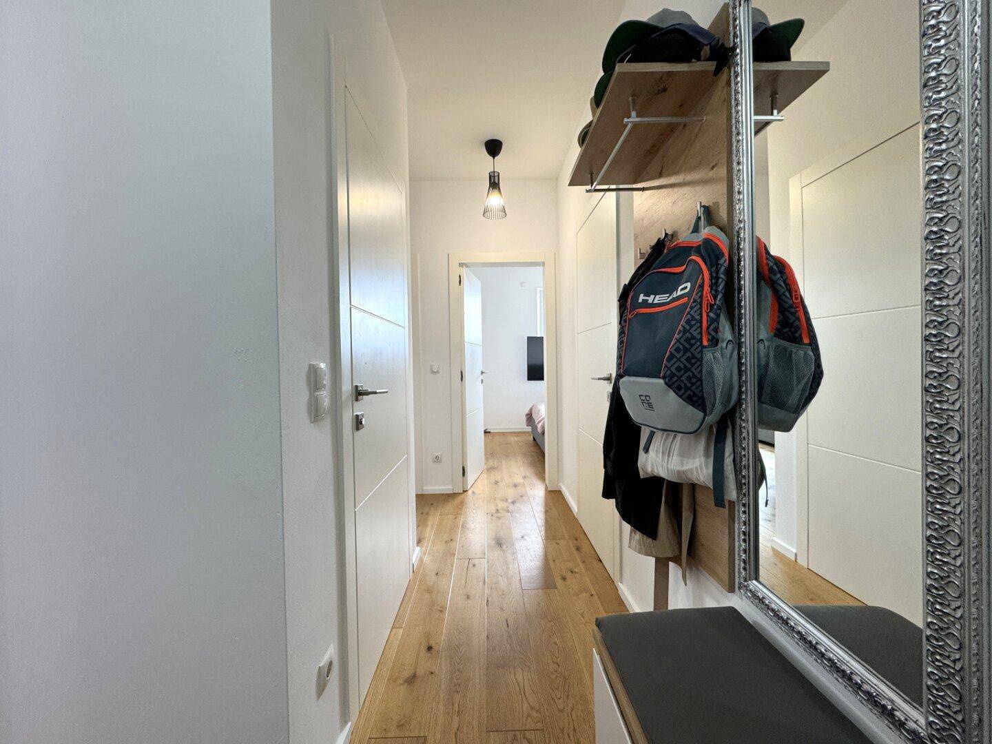 Heller Flur mit Holzparkettboden, Garderobe und großem Spiegel, der zu weiteren Räumen führt.