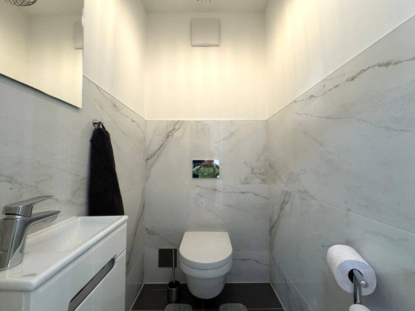 Stilvolles Gäste-WC mit wandhängender Toilette und modernen Marmor-Effektfliesen an den Wänden.