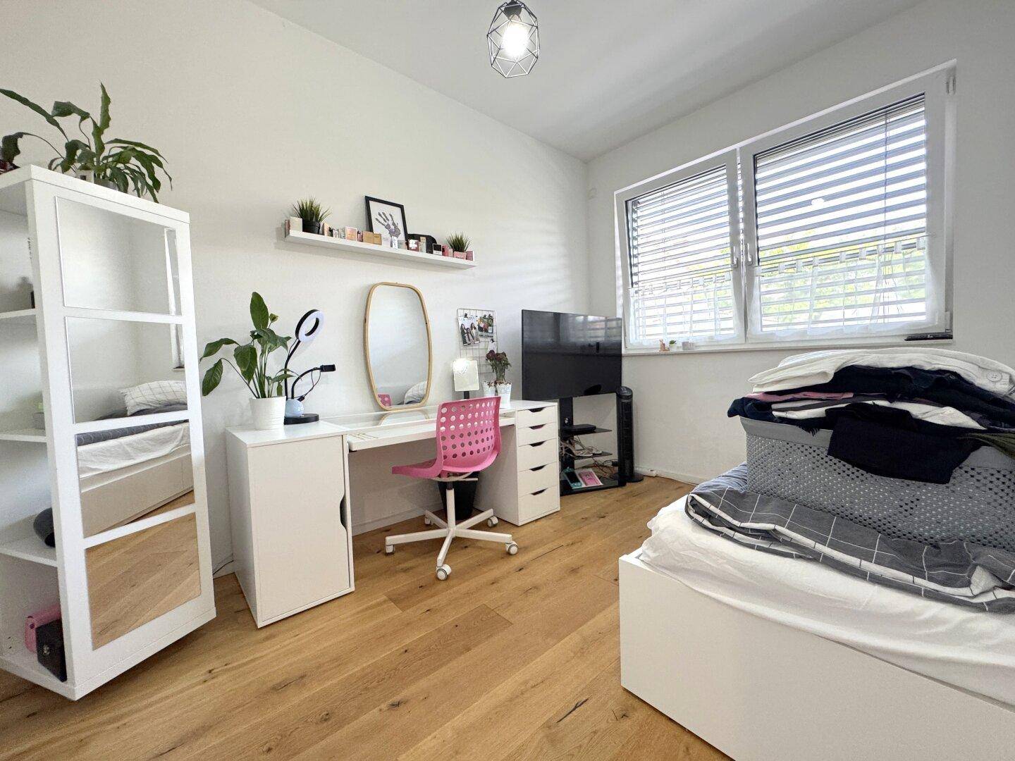 Helles Schlafzimmer mit Schreibtisch, Bett und großem Fenster, ideal als Jugend- oder Arbeitszimmer.