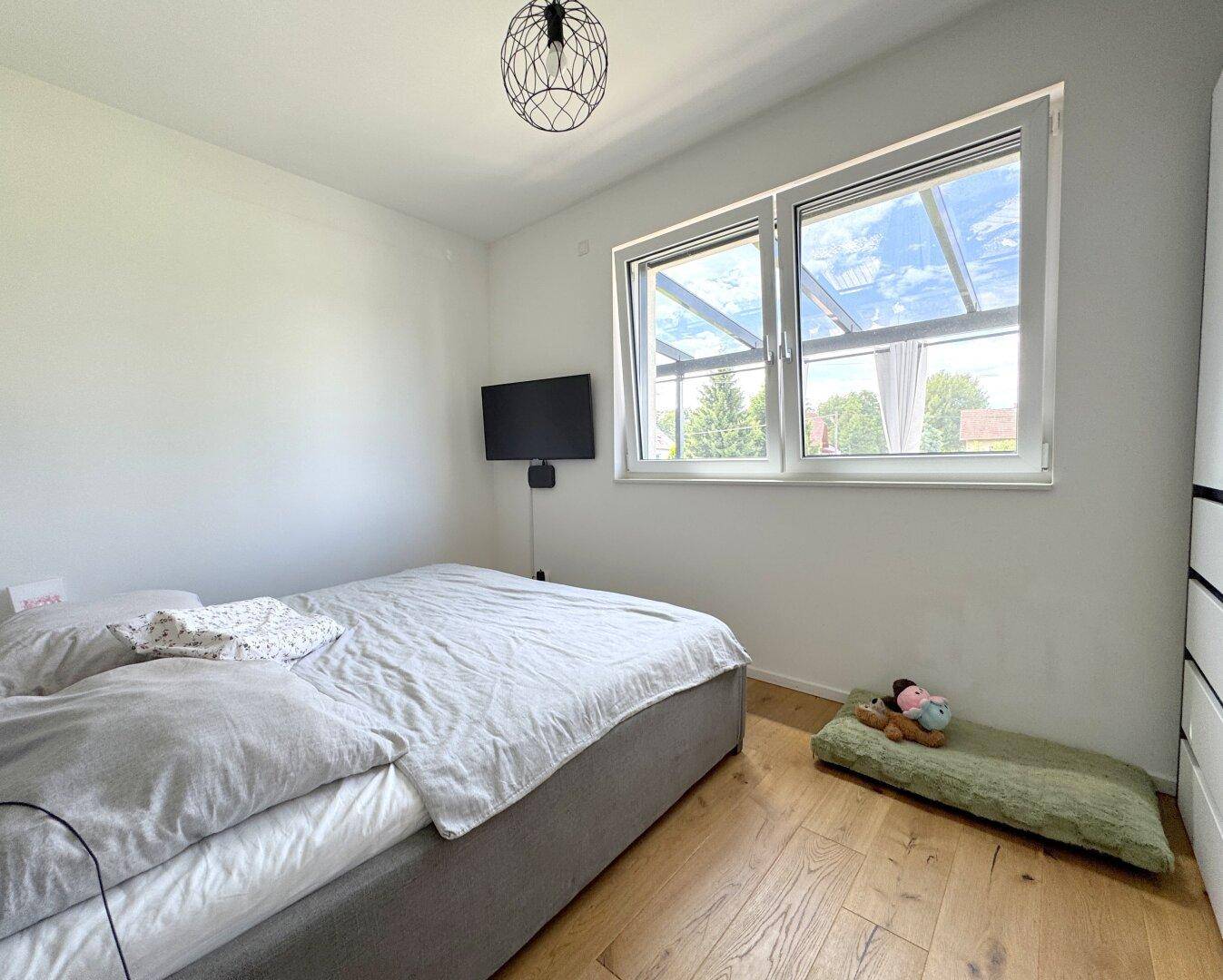 Helles Schlafzimmer mit Doppelbett und großem Fenster, das einen Blick ins Grüne bietet.