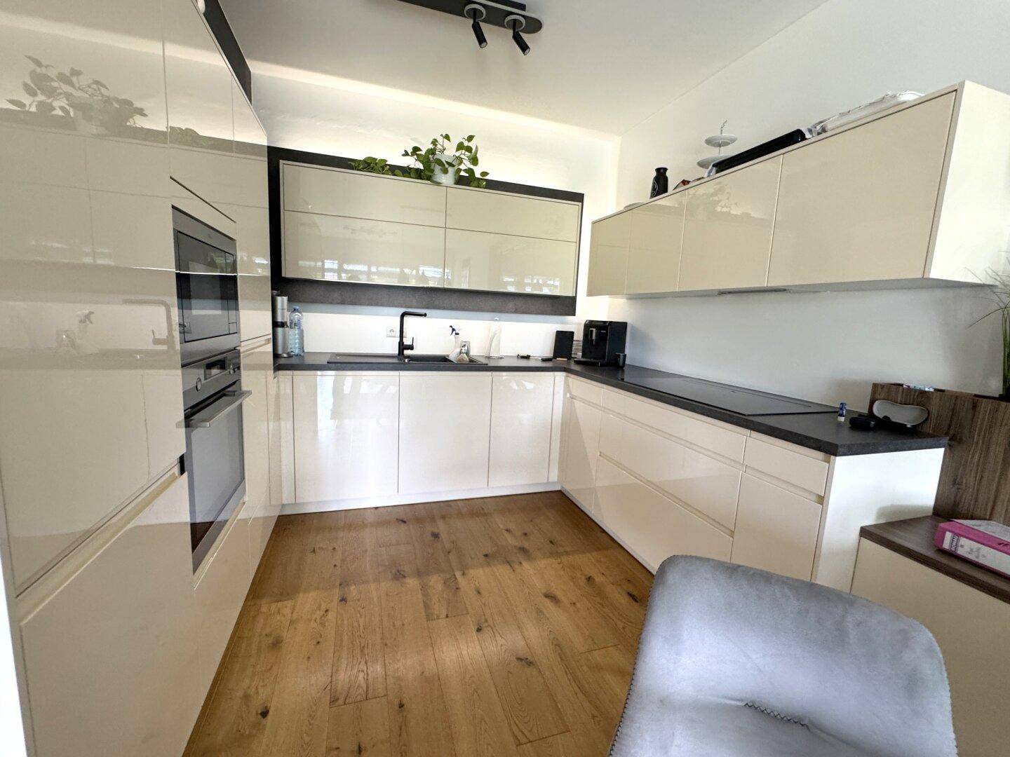 Moderne Einbauküche mit glänzenden cremefarbenen Fronten, integrierten Geräten und Holzparkettboden.