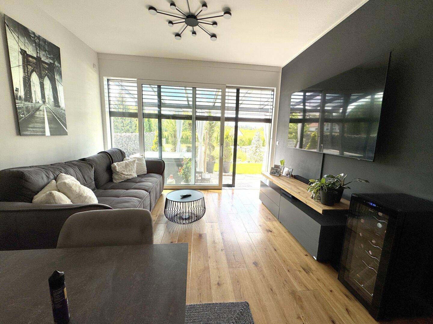 Gemütliches Wohnzimmer mit großem Sofa, Wandfernseher und Zugang zu einer sonnigen Terrasse.