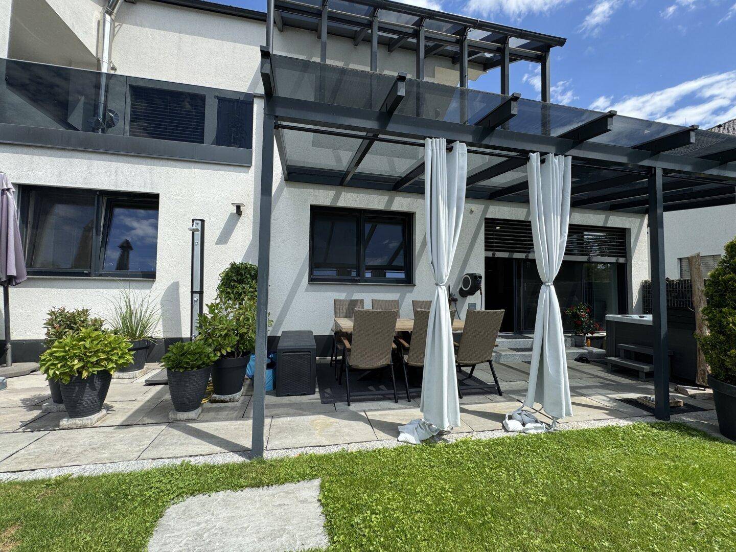 Überdachte Terrasse mit Esstisch und Stühlen, angrenzend an das Haus und einen gepflegten Rasen.