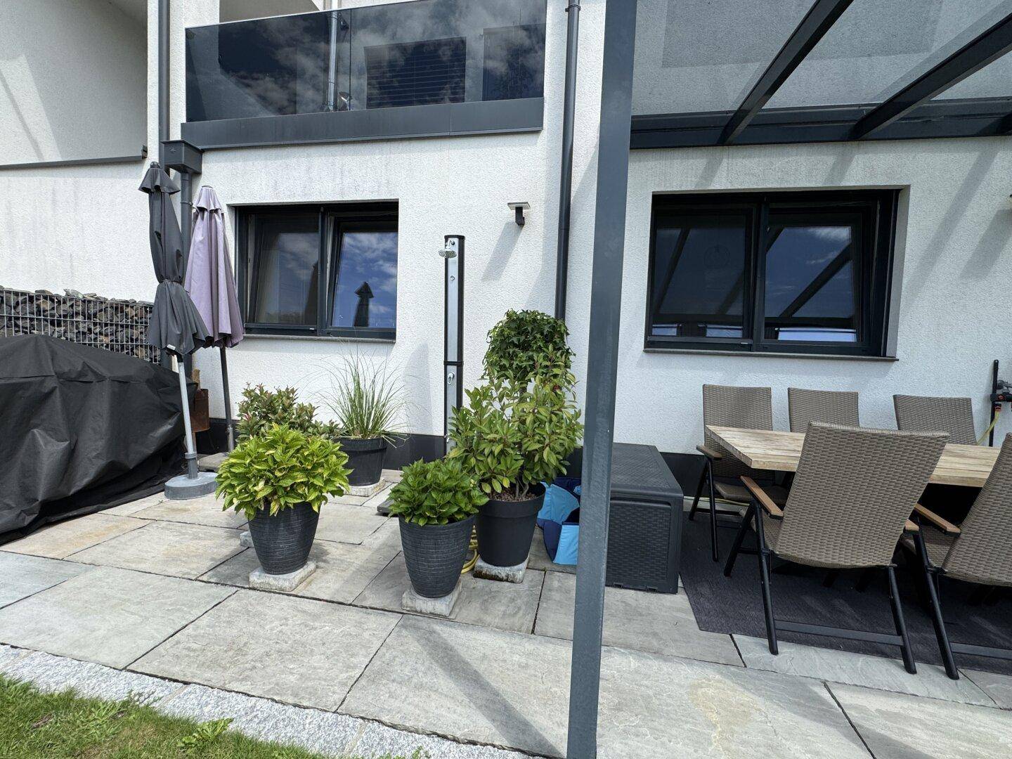 Gepflasterter Terrassenbereich mit verschiedenen Topfpflanzen und Sonnenschirm, ideal zum Entspannen.