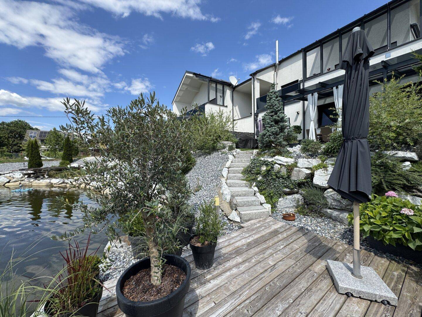 Modernes Haus mit großem Naturteich und Holzdeck, umgeben von einer liebevoll gestalteten Gartenanlage.