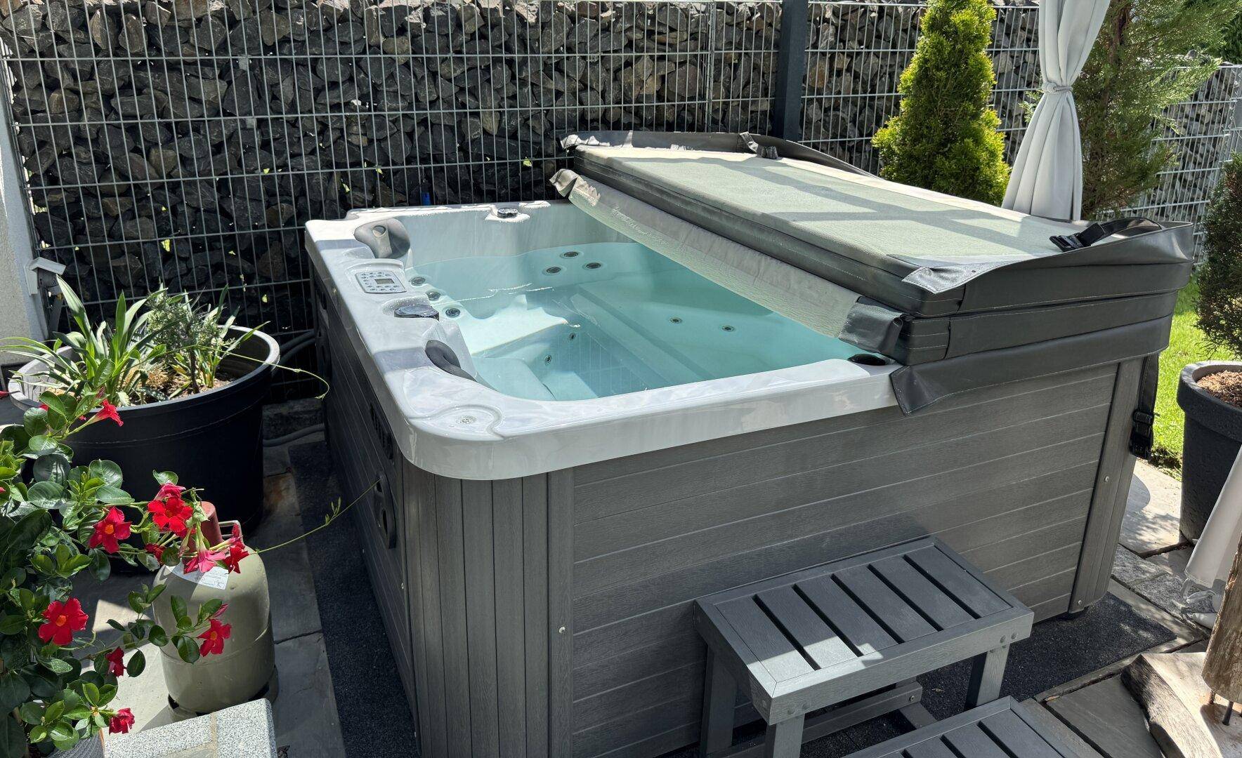 Entspannender Whirlpool im Gartenbereich, umgeben von Pflanzen und einer Gabionenwand.
