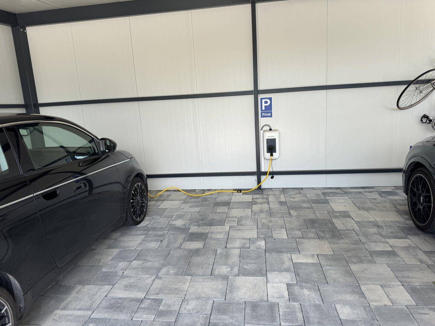 Überdachter Parkplatz mit Ladestation für Elektrofahrzeuge und gepflastertem Boden.