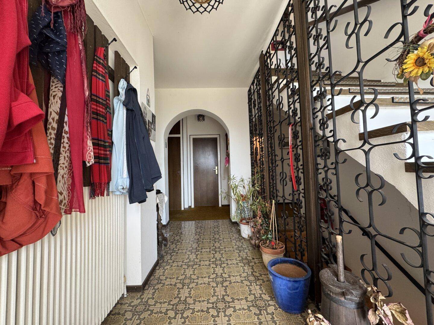 Eingangsbereich mit gemusterten Fliesen, schmiedeeisernem Treppengeländer und Garderobe.