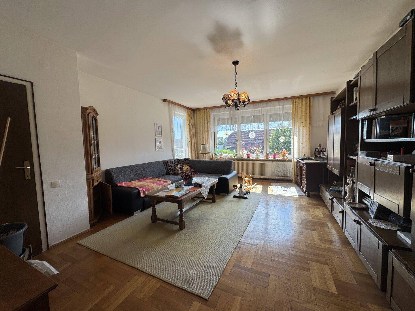 Helles Wohnzimmer mit Parkettboden, großem Fenster und traditionellen Holzmöbeln.