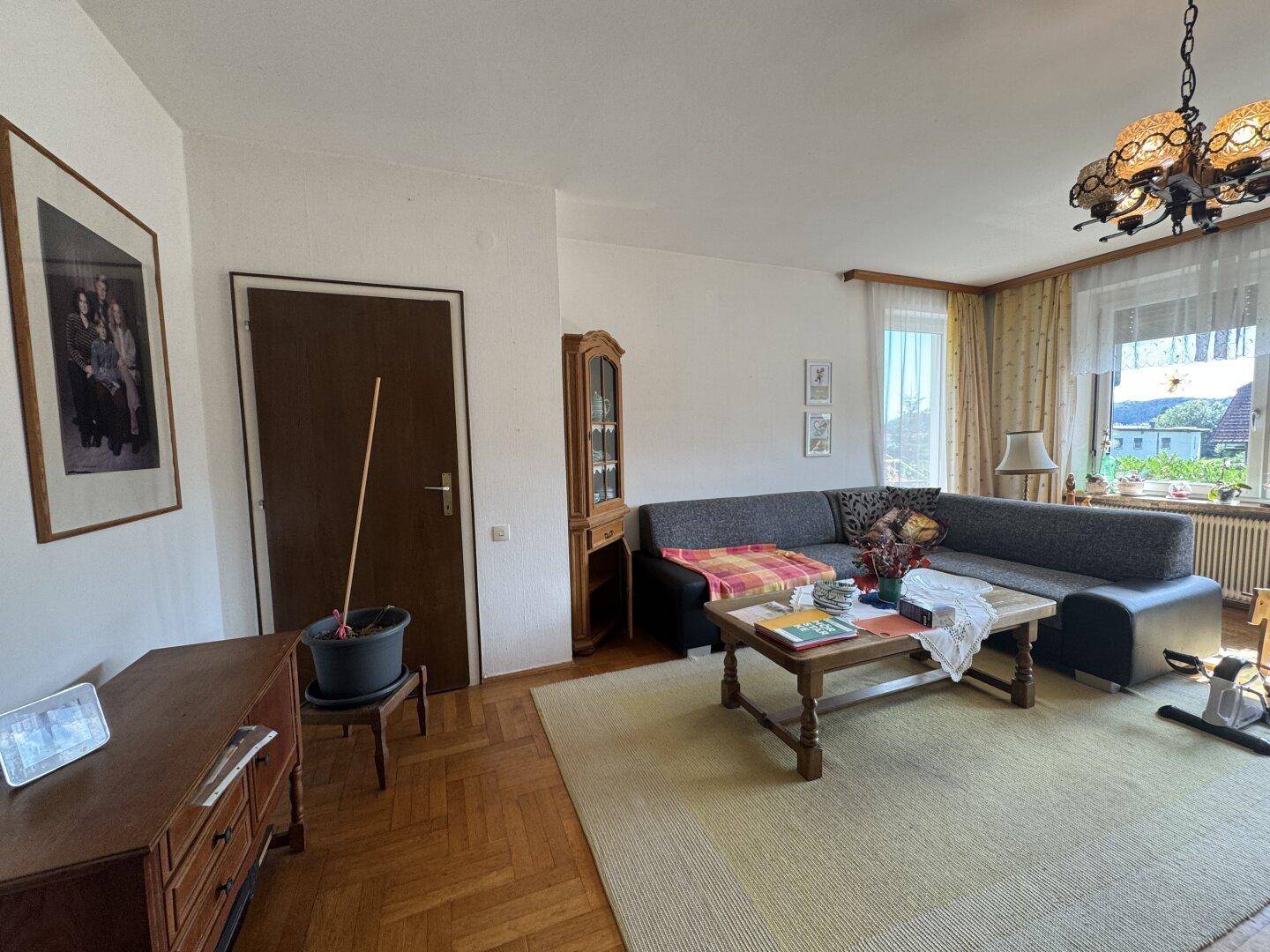 Gemütliches Wohnzimmer mit Parkettboden, Sofa und Blick ins Grüne durch das Fenster.